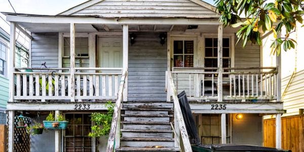 Old weathered wooden duplex with stairs and white picket fence.