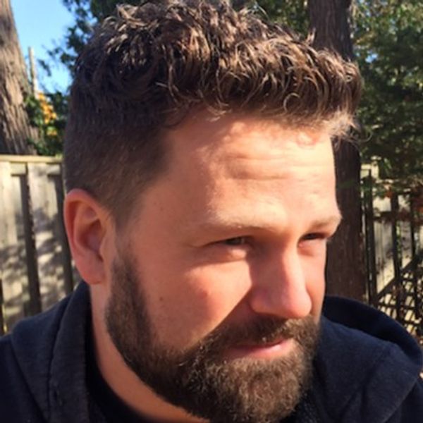 Man with curly hair and beard outdoors in sunlight.