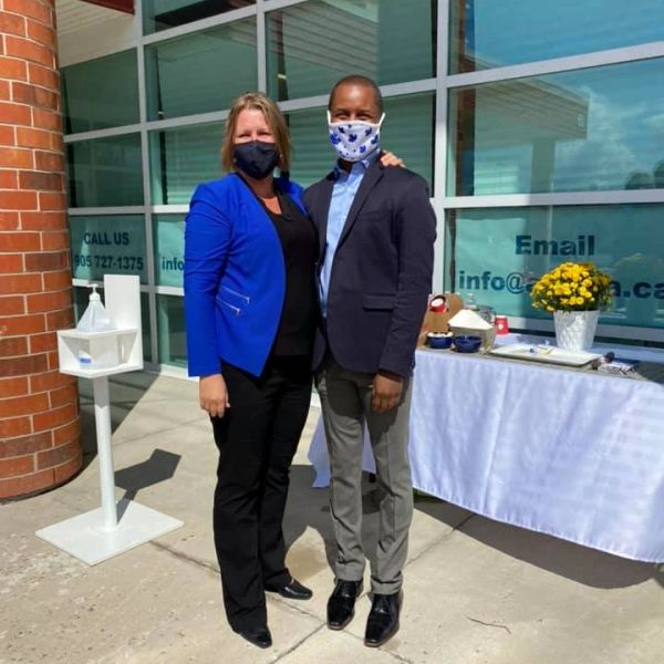 Two people wearing masks standing outside near a table with flowers and drinks.