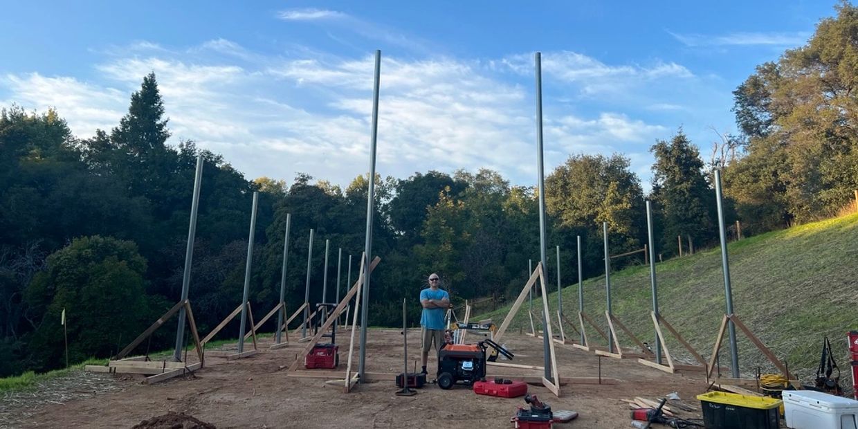 Person standing in a construction site with vertical metal poles.