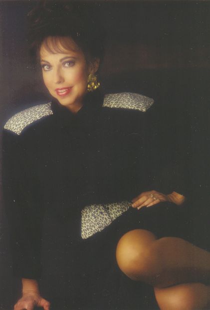 Woman in black dress with patterned accents posing.