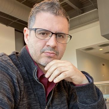 Man wearing glasses and a dark sweater sitting indoors.