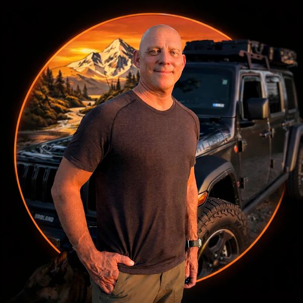 Man standing confidently with an off-road vehicle and mountain sunset background.