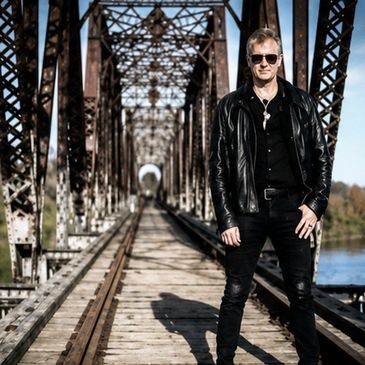 Man in black leather jacket standing on a metal bridge.