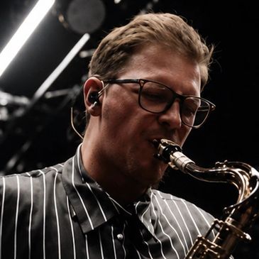 Man playing saxophone with glasses and striped shirt.