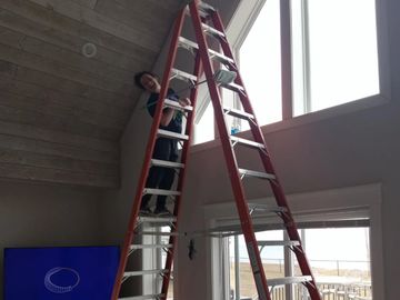 Person standing on a tall red ladder indoors near a large window.