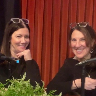 Two women smiling at a podcast or talk show setup with microphones.