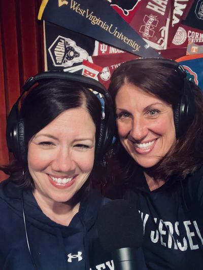 Two women wearing headphones and smiling, holding a microphone.
