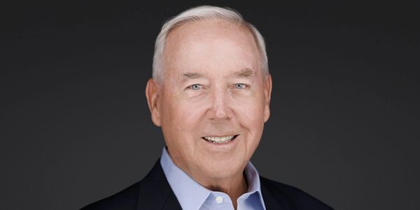 Portrait of a smiling elderly man in a suit against a dark background.