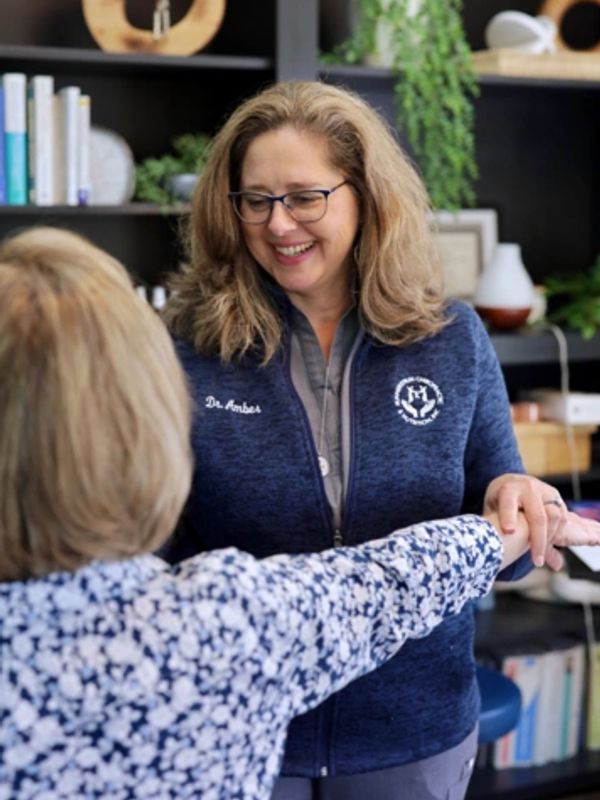 Woman in glasses smiling while holding another woman's arm in a cozy room.