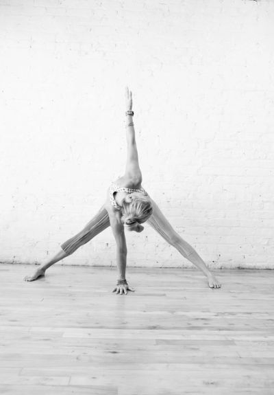 Woman performing a wide-legged yoga stretch against a white brick wall.