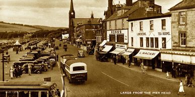 Black and white photo of a busy street with parked cars and shops.