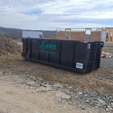 Large black dumpster at a construction site with a building framework in the background.