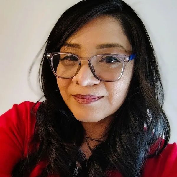 Woman with glasses and long dark hair wearing a red top, smiling softly.