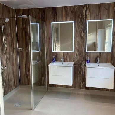 Modern bathroom with wooden textured walls, two illuminated mirrors, and a glass shower enclosure.we also sell wet rooms, mobility showers and walk in baths