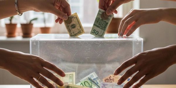 Hands putting money into a transparent donation box.