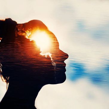 Silhouette of a woman with a sunrise and water reflection inside her profile.