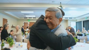 Two elderly men warmly hugging at a social gathering.