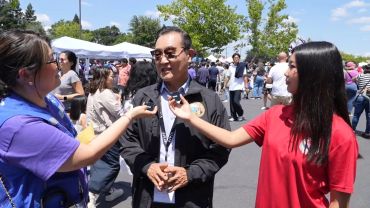 Two women interviewing a man outdoors at an event.