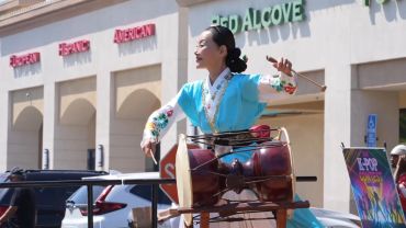 Woman in traditional outfit playing Korean drum outdoors.