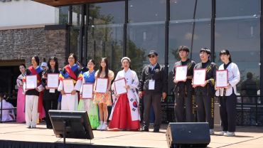 Group of people holding certificates on stage outdoors.