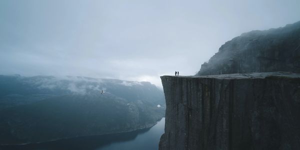 Two people standing on a cliff overlooking a foggy valley.