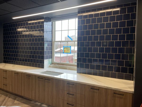 Modern kitchen backsplash with blue tiles and wooden cabinets beneath a window.