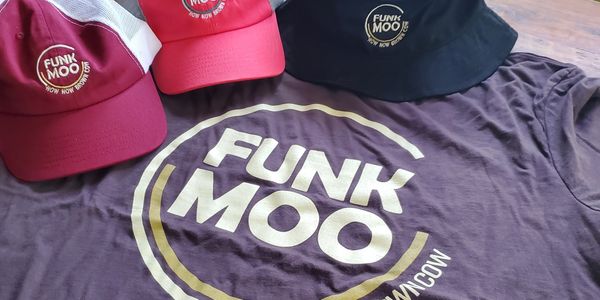 Caps and a t-shirt with 'Funk Moo' logo and slogan on a wooden surface.