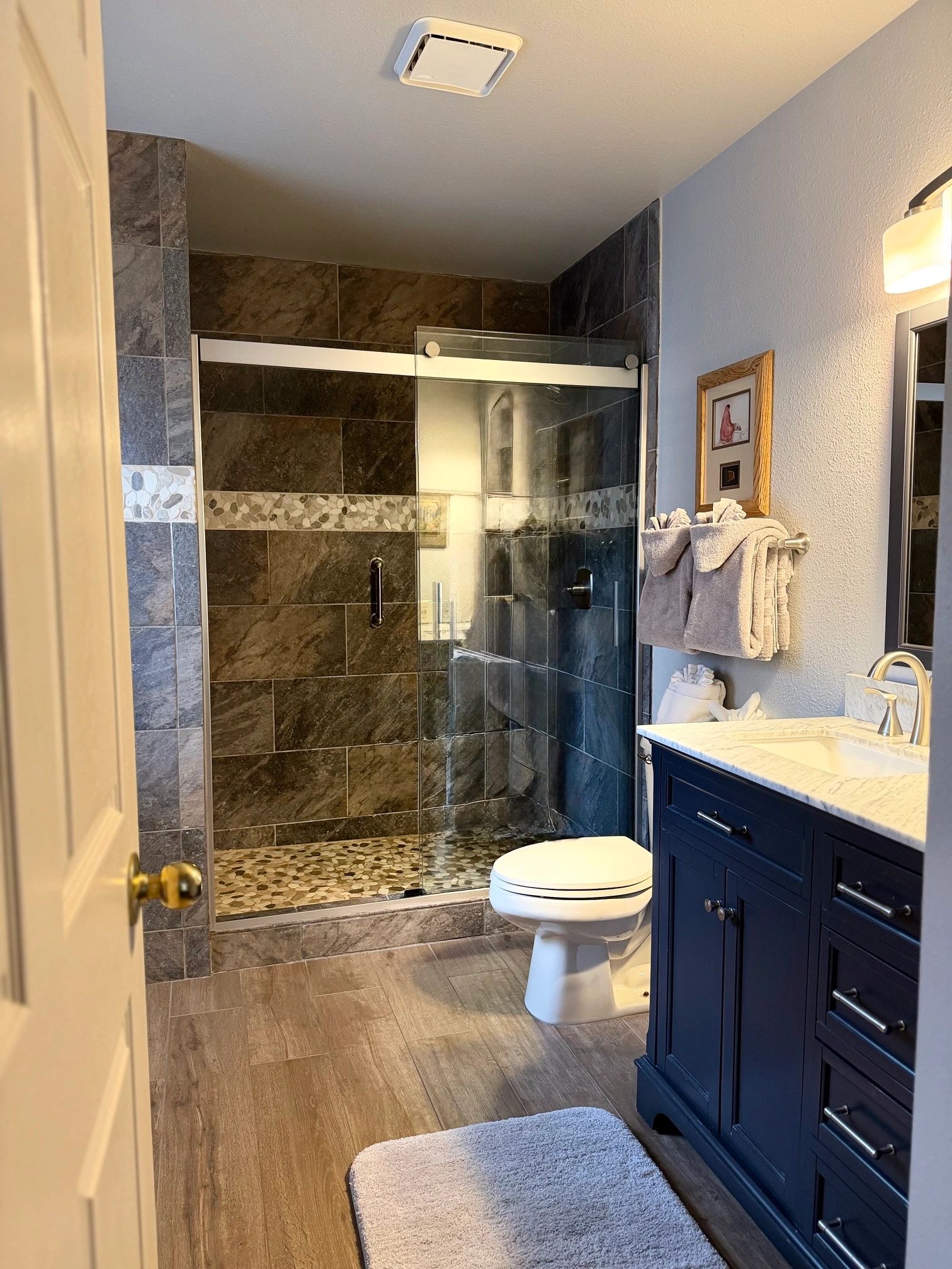 A clean and modern bathroom with a tiled shower, white toilet, and blue cabinet under a marble sink.