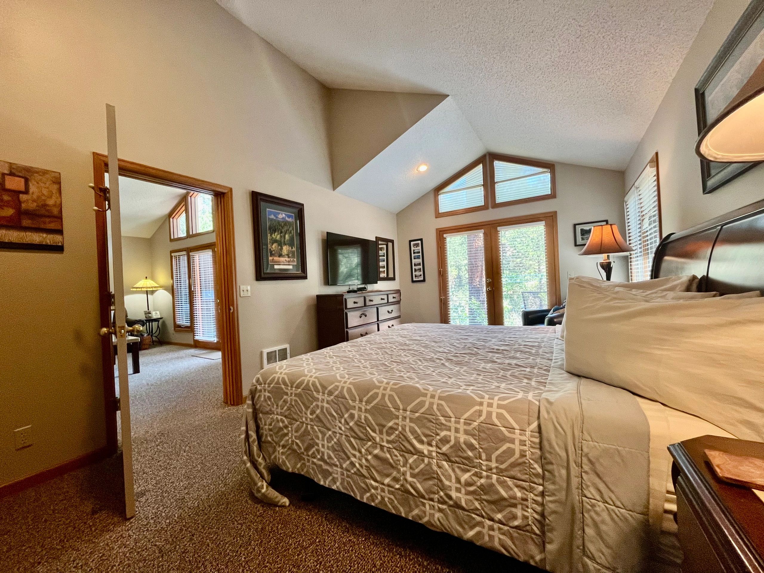 A hotel room with a bed, dresser, TV, and window