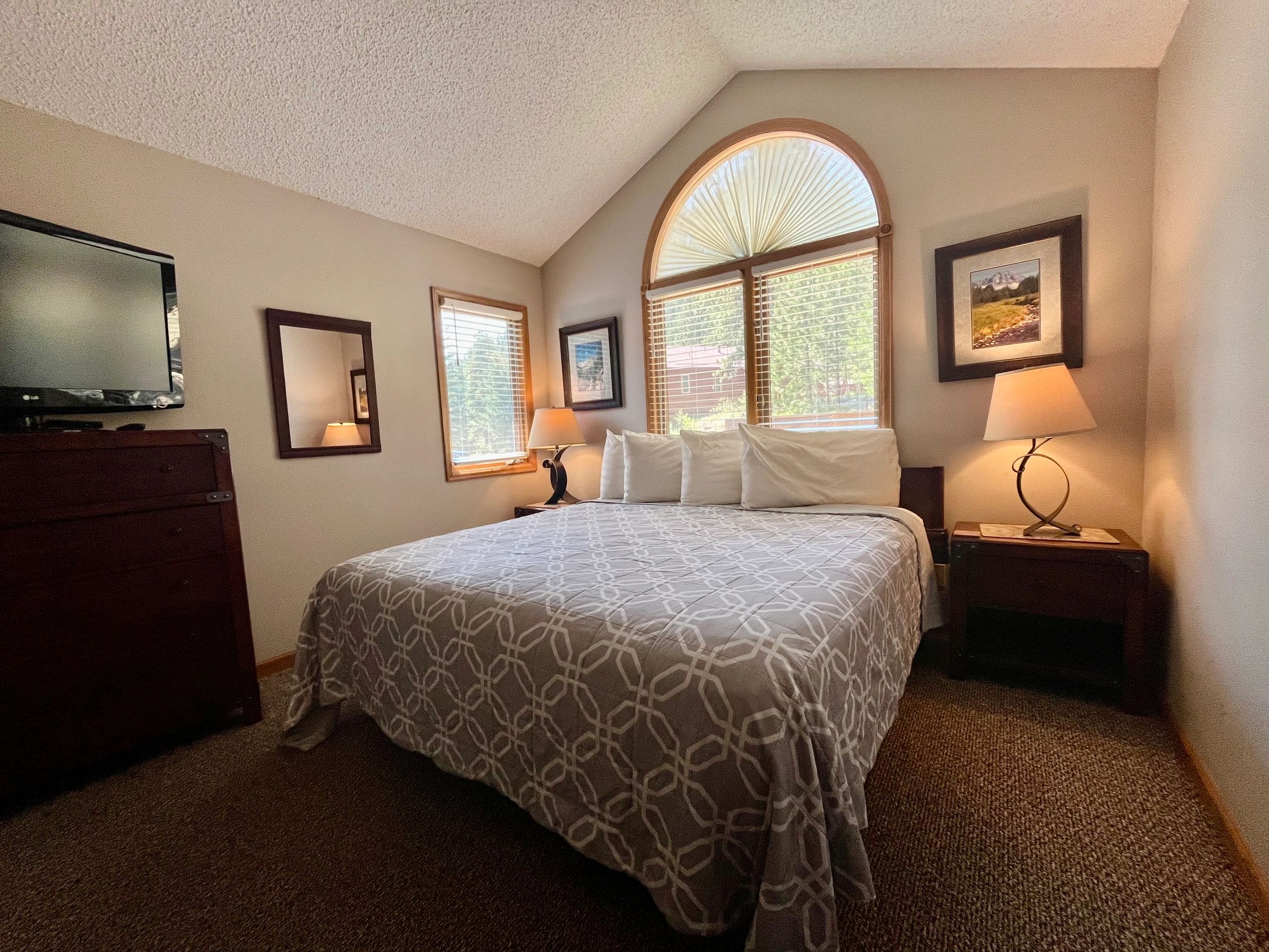A wide-angle view of a guest room with a bed, TV, and window