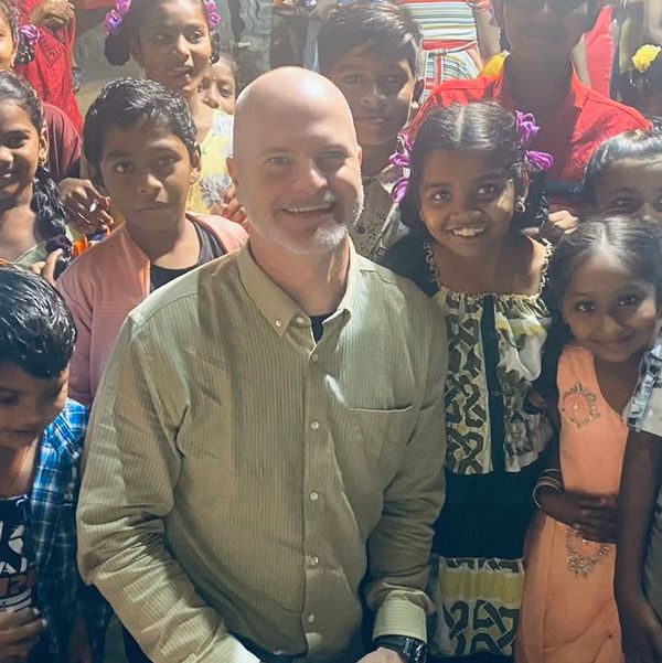 A man surrounded by smiling children in a lively setting.