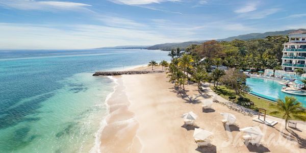 Tropical beach resort with clear blue waters and palm trees under a sunny sky.