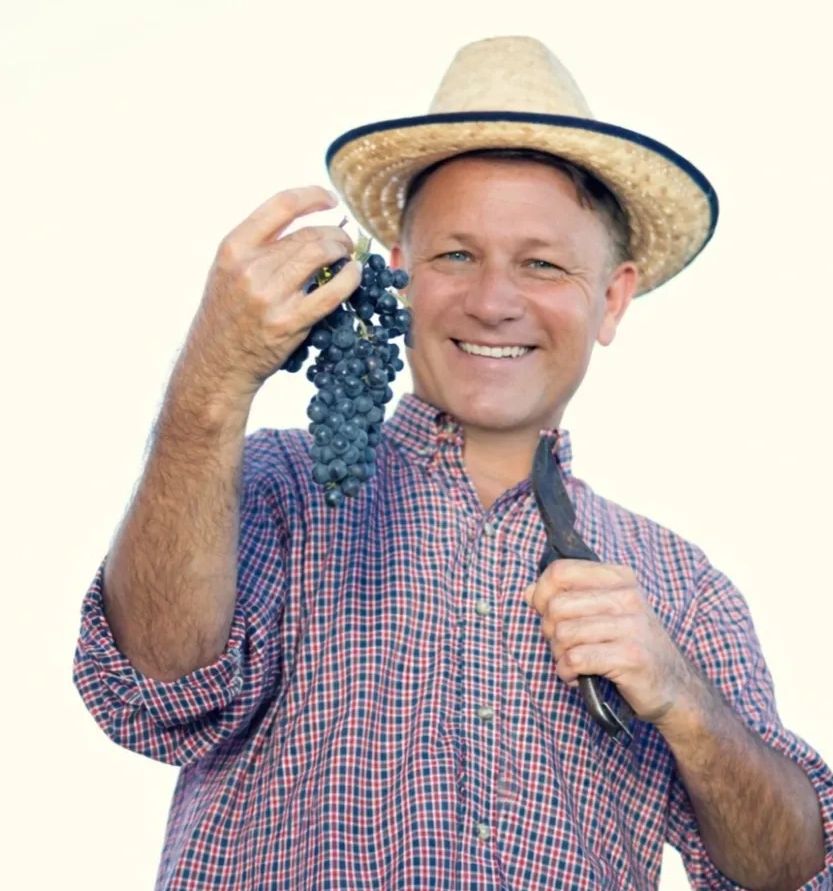 Smiling farmer in straw hat holding grapes and pruning shears.