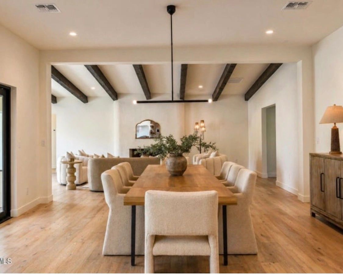 Modern dining room with wooden table and cozy beige chairs under black pendant light.
