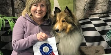 Woman with a dog holding a first-place ribbon at a dog sports event.