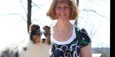 A smiling woman with a fluffy dog outdoors on a sunny day.