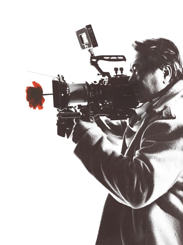 Person aiming a camera with a red flower attached to the lens.