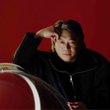 Man in black jacket posing against a red background.