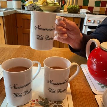 Three white mugs with text on a wooden table, one being held by a hand.