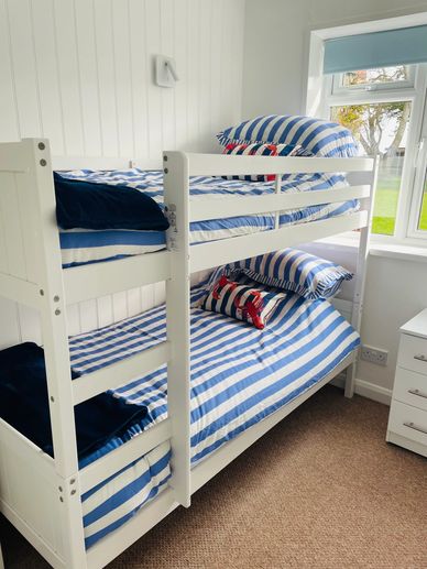 White bunk bed with blue and white striped bedding in a bright room.