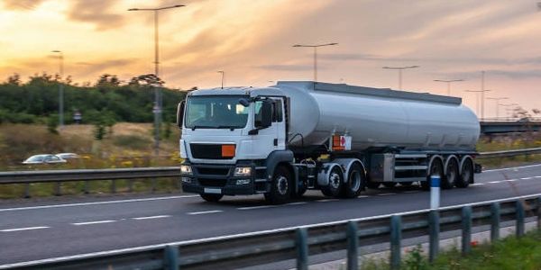 White tanker truck driving on a highway during sunset.