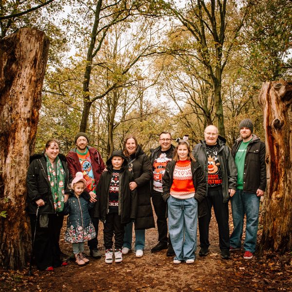 A family group wearing festive sweaters posing in a sherwood forest during autumn.