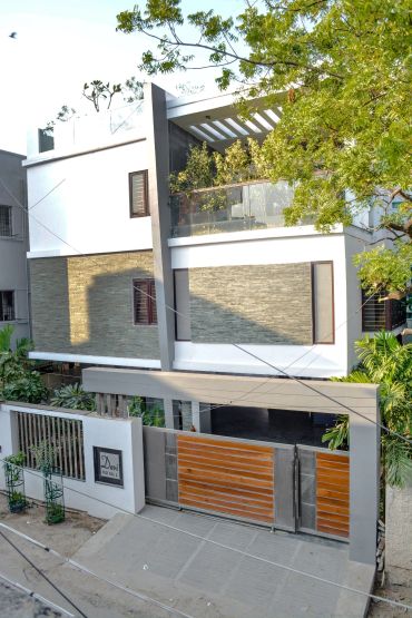 Modern three-story house with a wooden gate and greenery.