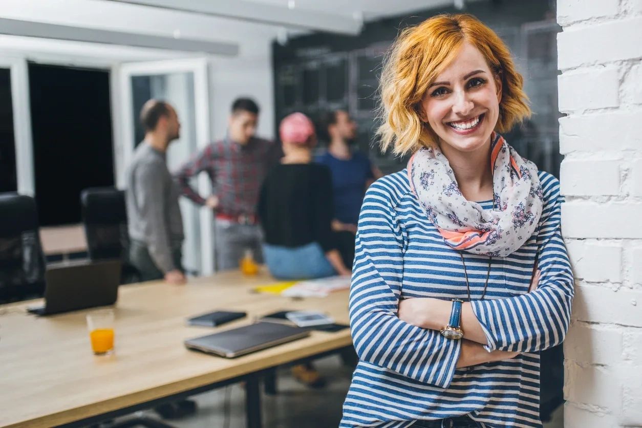 woman leaning against wall with work space behind her, strategy is all about, systems strategy, 