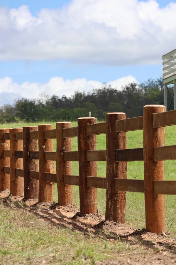 Rustic wooden fence posts in a green field under a partly cloudy sky.