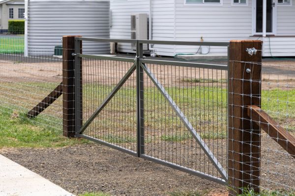 Metal farm gate with wire fencing and wooden posts at a rural property.