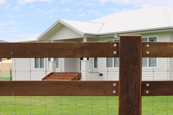 Wooden fence in front of a white house with a green lawn.