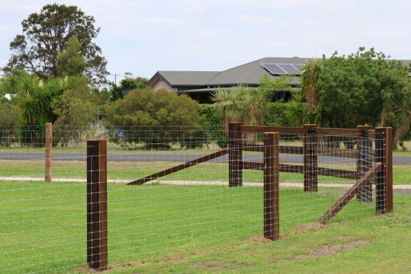 A wire fence with wooden posts in front of a house with solar panels.