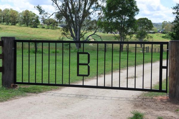 Black metal gate with letter B on a rural dirt road.